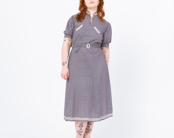 May include: A gray vintage dress with short sleeves, a high collar, and a belted waist. The dress features white trim on the collar, pockets, and hem. The dress is knee-length and has a subtle checkered pattern.