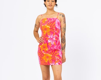May include: A vibrant pink mini dress with a floral pattern featuring orange and yellow flowers. The dress has thin spaghetti straps and a square neckline. The model is standing in front of a white background.