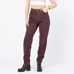 May include: Dark burgundy denim jeans with a classic five-pocket design. The jeans have a straight leg cut and a button and zipper closure. The model is wearing black leather boots with a block heel.