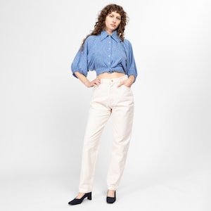 Puede incluir: Una mujer con una camisa azul claro con cuello, anudada a la cintura y pantalones de color crema de cintura alta.