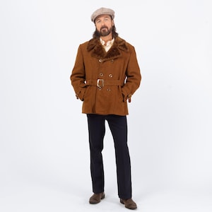 Peut inclure: Un manteau en laine marron avec un col en fausse fourrure et une ceinture. Le manteau a un design croisé avec des boutons dorés et une boucle de ceinture assortie. La personne porte un pantalon bleu foncé et une casquette en tweed.