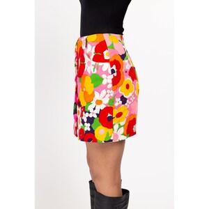 May include: A pink mini skirt with a colorful floral print. The skirt has a button closure and a high waist.