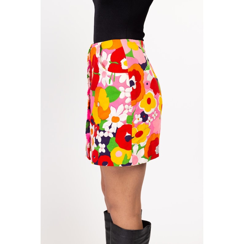 May include: A pink mini skirt with a colorful floral print. The skirt has a button closure and a high waist.