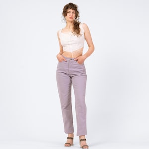 May include: A woman wearing a light pink crop top and lavender-colored pants. The top has a square neckline and tie detail. The pants are high-waisted and straight-legged. The woman is also wearing high-heeled sandals.