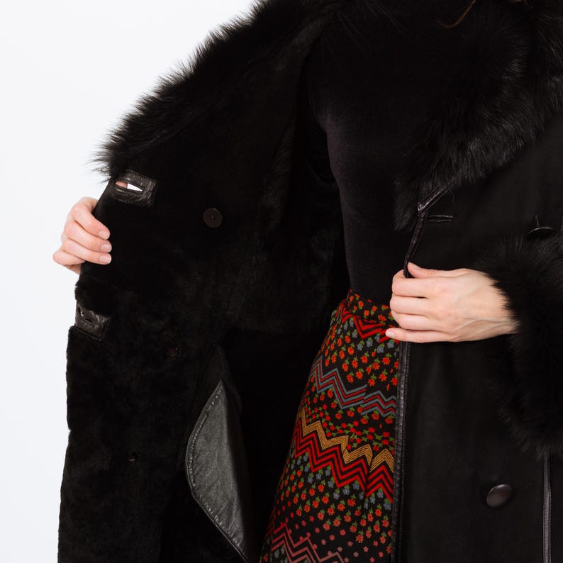 May include: Black shearling coat with a fur collar and cuffs. The coat has a double-breasted design with leather accents and a plush interior. The coat is open, revealing the interior lining and a patterned skirt.