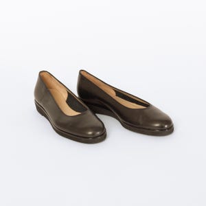 May include: A pair of black leather wedge-heeled shoes. The shoes have a rounded toe and a low wedge heel. The interior is a light tan color. The shoes are displayed on a white background.