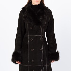 May include: A black double-breasted coat with a faux fur collar and cuffs. The coat features dark brown buttons and trim. The long coat is made of a suede-like material and is designed for cold weather.