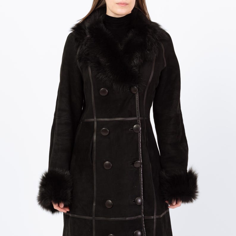 May include: A black double-breasted coat with a faux fur collar and cuffs. The coat features dark brown buttons and trim. The long coat is made of a suede-like material and is designed for cold weather.