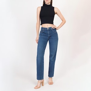 May include: A person wearing a black mock neck crop top and blue straight leg jeans. The person is wearing nude heeled sandals.