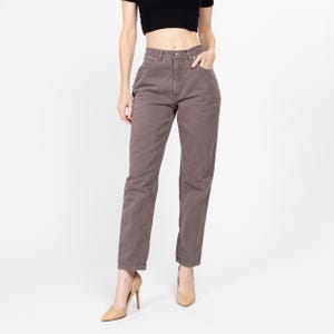 Puede incluir: Un par de pantalones vaqueros de tiro alto y pierna recta de color marrón oscuro. Los vaqueros tienen un diseño clásico de cinco bolsillos y cierre de botón.