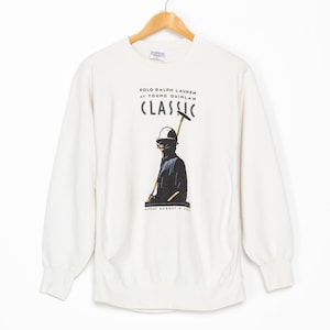 May include: White long-sleeve sweatshirt with a graphic print of a polo player holding a mallet. The text "Polo Ralph Lauren at Young Quinlan Classic" is printed on the sweatshirt.