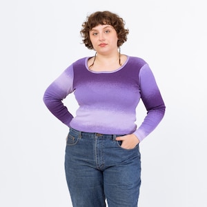 May include: A woman wearing a purple ombre long-sleeve shirt with a scoop neck and blue jeans.
