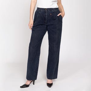 Peut inclure: Pantalon en jean délavé foncé à taille haute et plis. Le pantalon a une coupe droite et un petit détail brodé près du bouton. Le modèle porte des talons noirs. Un style classique.
