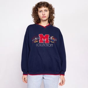 May include: A navy blue sweatshirt with a red and white embroidered Mickey Mouse "M" Collection logo.