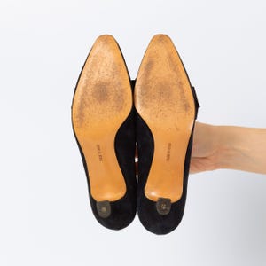 Puede incluir: Un par de tacones negros de ante con tac&oacute;n bajo y punta afilada. Las suelas son de color marr&oacute;n claro y muestran desgaste. Los tacones se sostienen sobre un fondo blanco. Las palabras "MADE IN ITALY" est&aacute;n impresas en las suelas.