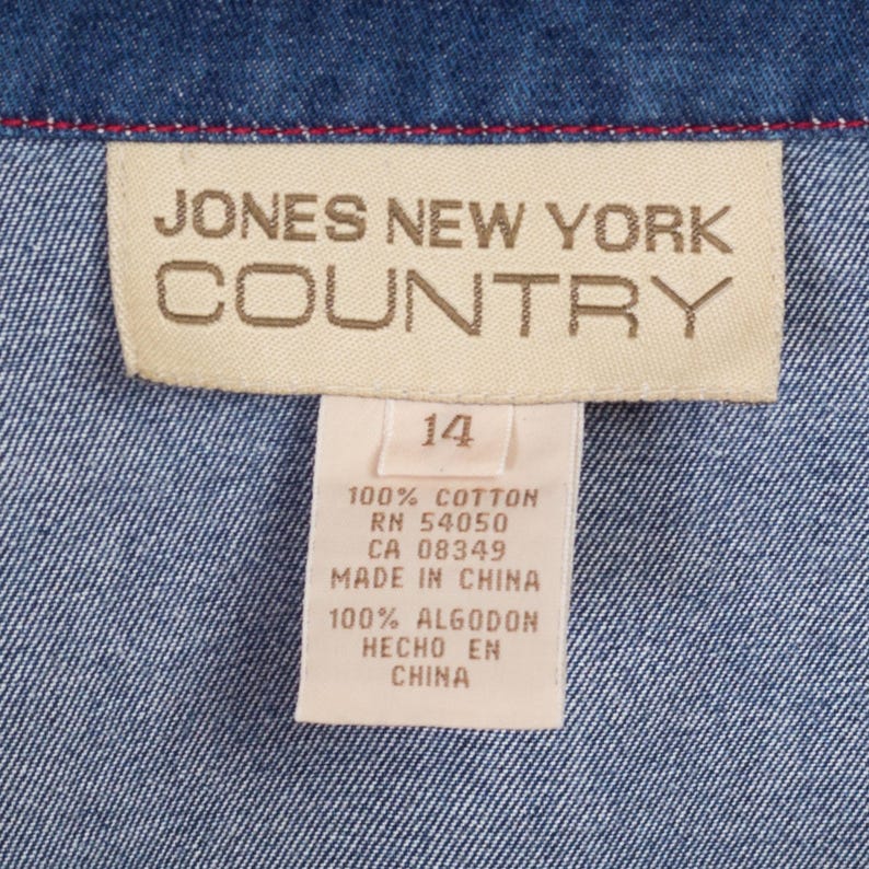 May include: A tan label with the text "JONES NEW YORK COUNTRY" in brown lettering. Below the label is a smaller white label with the text "14" in black lettering. The smaller label also has the text "100% COTTON RN 54050 CA 08349 MADE IN CHINA 100% ALGODON HECHO EN CHINA" in black lettering.