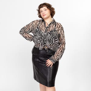 May include: A woman wearing a black and white zebra print sheer blouse tied at the waist and a black leather skirt.