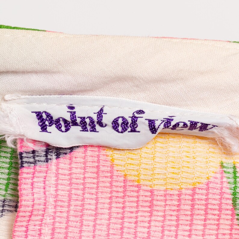 May include: Close-up of a white fabric label with purple embroidered text that reads "Point of View" on a colorful patterned fabric.