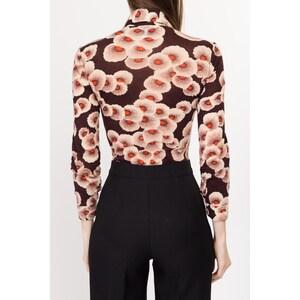 May include: A long-sleeved, brown turtleneck top with a floral print featuring white and orange flowers. The top is fitted and has a high neckline.