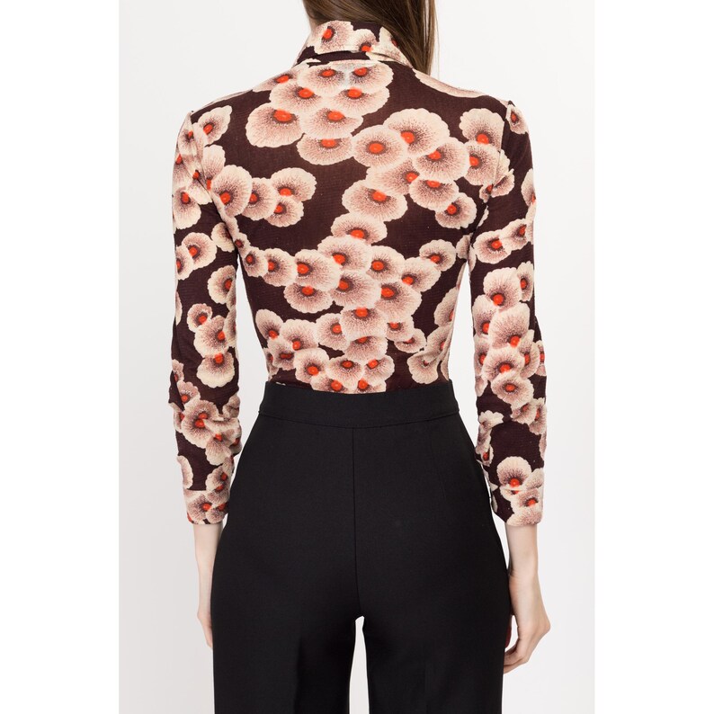 May include: A long-sleeved, brown turtleneck top with a floral print featuring white and orange flowers. The top is fitted and has a high neckline.