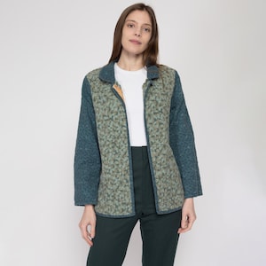 May include: A teal blue and green patterned jacket with a zipper closure and a collar. The jacket has a floral pattern on the front and sleeves.