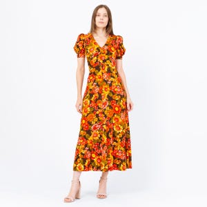 May include: A vintage-style midi dress with a vibrant floral pattern in shades of orange, yellow, and red. The dress features a V-neckline, short puff sleeves, and a flowing skirt. The model is wearing nude-colored heels.