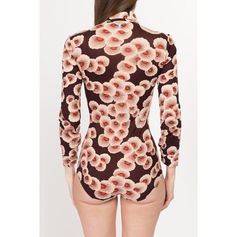 May include: A long-sleeved bodysuit with a brown background and a floral pattern in shades of white, orange, and red.