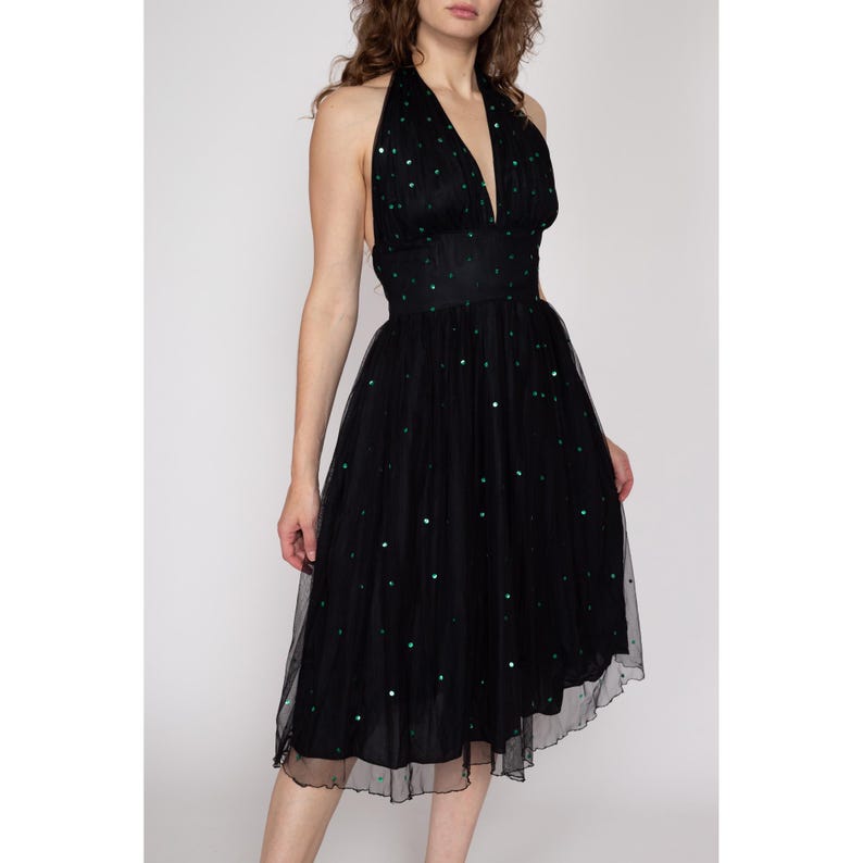 May include: A black tulle halter dress with green sequins. The dress has a fitted bodice and a flowing skirt.