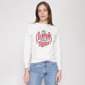 Peut inclure: Sweat-shirt blanc avec un imprimé graphique rouge, bleu et vert qui dit "1987 World Series Champions Minnesota Twins".