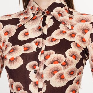 May include: A brown long-sleeved shirt with a white and orange floral pattern. The shirt has a button-up collar and a button-down front.