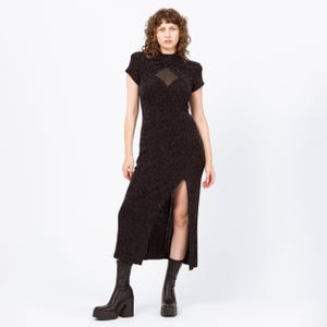 Puede incluir: Vestido marrón oscuro hasta la rodilla con cuello alto y mangas cortas. El vestido presenta un panel transparente en el pecho y una abertura en el muslo. La modelo lleva botas de plataforma negras.