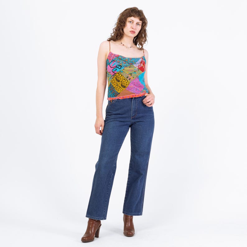 Puede incluir: Una mujer con un top de tirantes con estampado de patchwork colorido y vaqueros azul oscuro. El top presenta una variedad de patrones y colores, incluyendo rosa, amarillo y azul. Tambi&eacute;n lleva botines marrones.