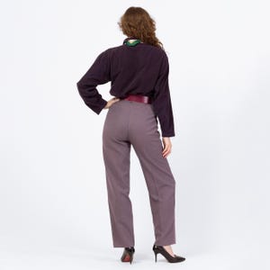 May include: A person wearing a dark purple long-sleeve shirt, mauve pants, and a burgundy belt. The person is also wearing black high heels. A green and white scarf is visible at the neck.