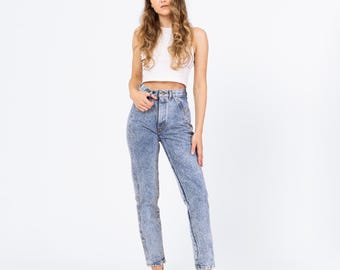 May include: A woman in a white crop top and acid wash jeans. The jeans are high-waisted with a button and zip fastening. She is also wearing beige heels.