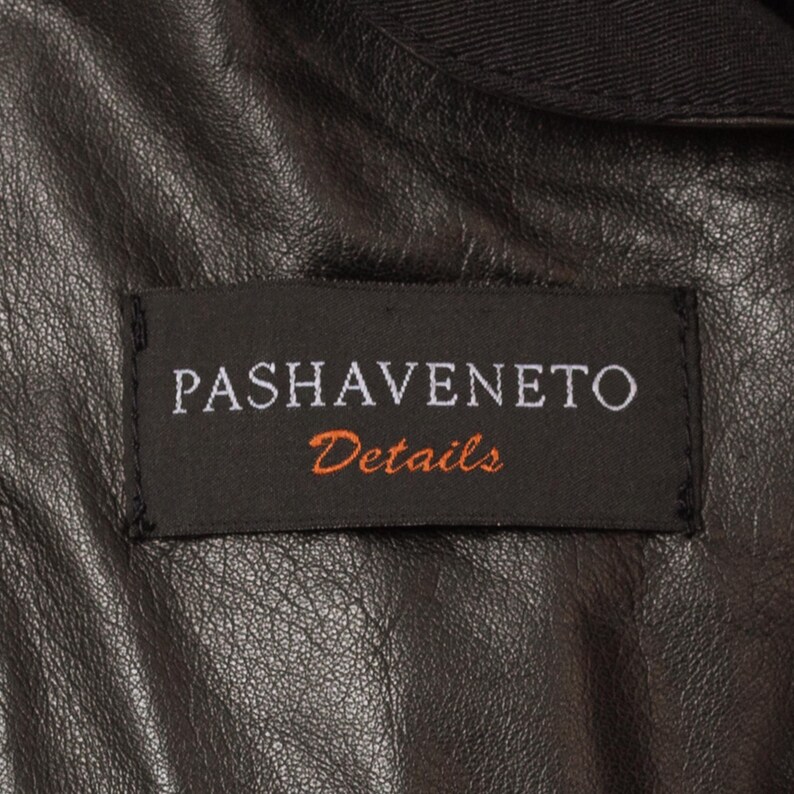 May include: Close-up of a black leather jacket with a label that reads "PASHAVENETO Details" in white and orange lettering. The jacket's leather has a textured appearance.