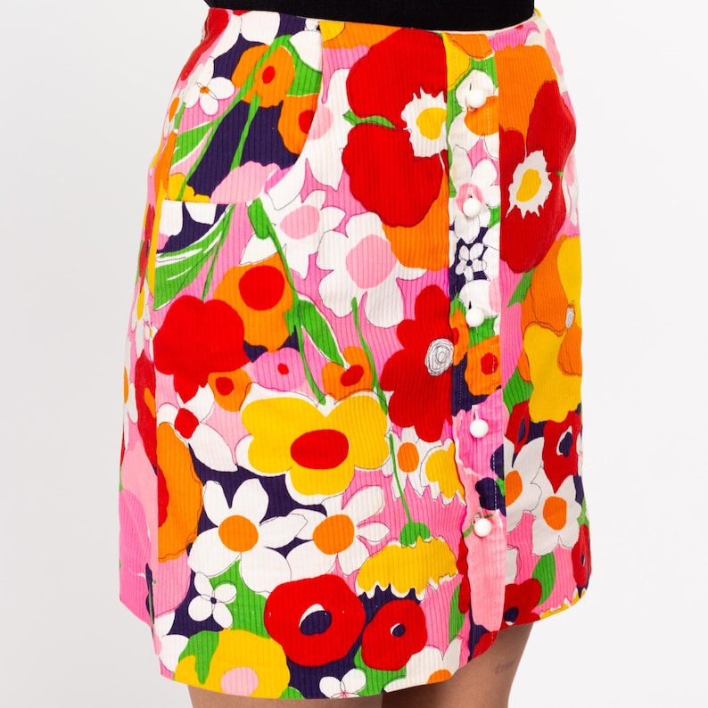 May include: A pink mini skirt with a colorful floral print. The skirt has a button closure and a patch pocket.