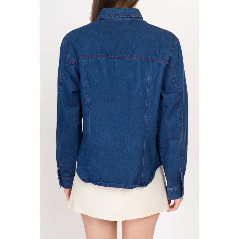 May include: A dark blue denim shirt with long sleeves and a button-up front. The shirt has a contrasting red stitching detail around the collar, pockets, and cuffs.