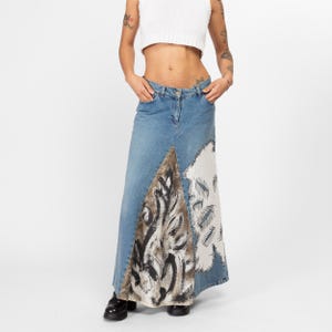May include: A long denim skirt with a patchwork design. The skirt is blue with white and brown accents. The skirt is made of denim and has a high waist.