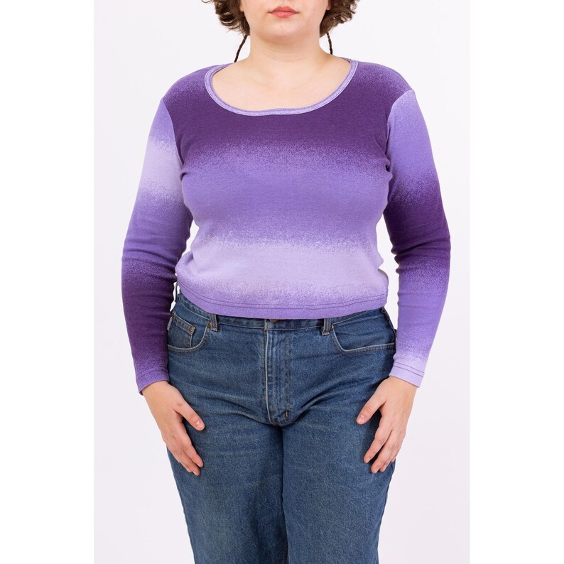 May include: A long-sleeved shirt with a purple ombre design. The shirt has a scoop neck and is made of a soft, stretchy fabric.