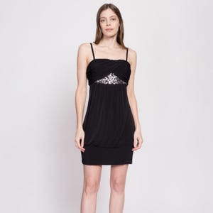Puede incluir: Un vestido negro sin mangas con un detalle de lentejuelas en la cintura.