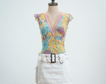 May include: A sleeveless top featuring a multi-colored floral pattern in shades of yellow, blue, and pink with a V-neckline trimmed in pink lace, paired with a white mini skirt that includes a wide belt with a black buckle and side pockets.