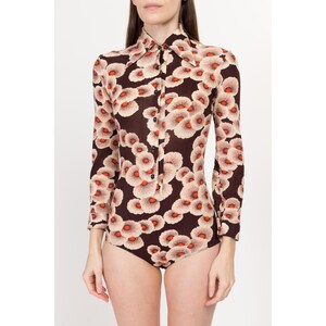 May include: A long-sleeved bodysuit with a brown background and a white and orange floral print. The bodysuit has a collared neckline and button closure.