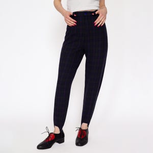 May include: Black and purple plaid pants with a high waist and a button closure. The pants have a unique design with the legs ending in a point at the ankle.