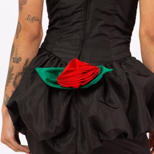 Może przedstawiać: Czarna sukienka z dużą czerwoną r&oacute;żą i zielonymi liśćmi z tyłu.
