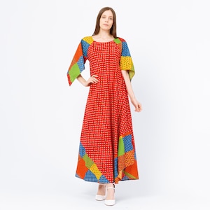May include: A red maxi dress with a small white dot pattern. The dress features patchwork sleeves and hem in blue, yellow, green, and orange. The dress has a round neckline and a flowing silhouette.
