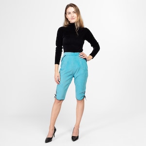 May include: A woman wearing a black turtleneck sweater and blue corduroy shorts with black trim and lace-up details. She is wearing black heels.