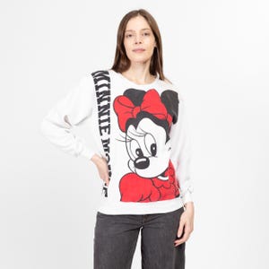May include: White long-sleeve sweatshirt with a black and white image of Minnie Mouse wearing a red bow and red dress. The text "MINNIE MOUSE" is printed vertically on the left side of the image.