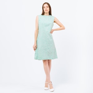 Puede incluir: Un vestido sin mangas, de largo hasta la rodilla, con estampado floral verde y blanco. El vestido tiene un escote redondo y una silueta ajustada.