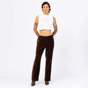 Peut inclure: Un haut court sans manches blanc associé à un pantalon en velours marron. Le pantalon a une coupe droite et une fermeture boutonnée et zippée. La tenue est portée avec des chaussures marron.