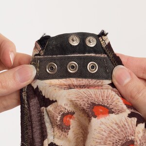 May include: Close-up of a black fabric with a row of silver metal hooks and a floral print. The fabric has a brown and white floral pattern with red accents.